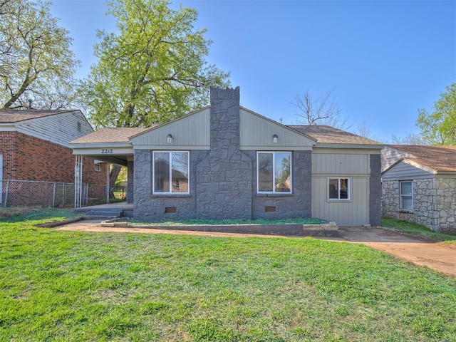 back of house featuring fence, a lawn, stone siding, and roof with shingles