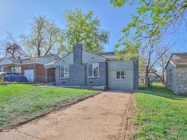 view of front of house featuring stone siding, a front yard, fence, and an attached garage