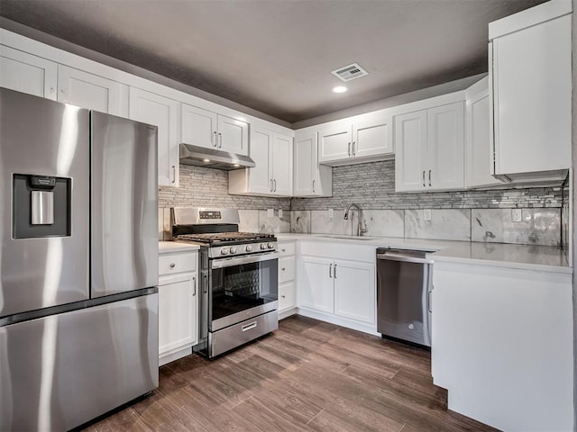 kitchen with light countertops, stainless steel appliances, dark wood-type flooring, under cabinet range hood, and a sink