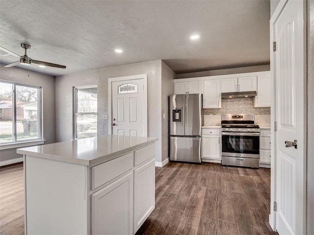 kitchen with light countertops, under cabinet range hood, decorative backsplash, dark wood finished floors, and appliances with stainless steel finishes