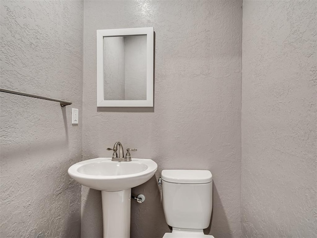 half bathroom with toilet and a textured wall