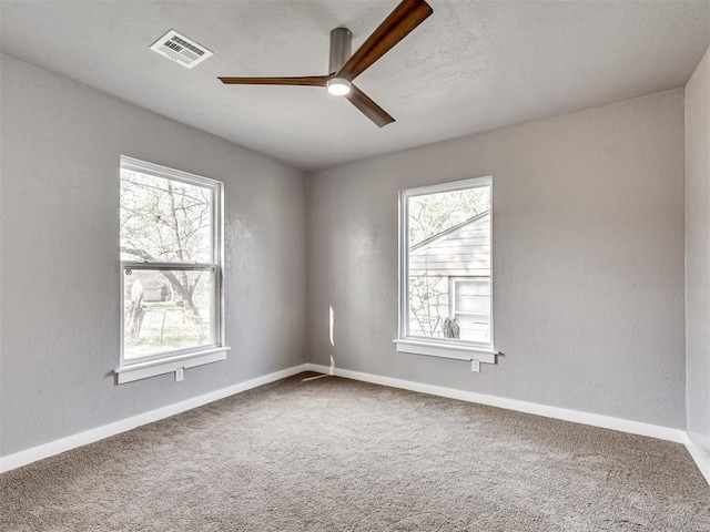 empty room featuring visible vents, carpet floors, a textured wall, and a ceiling fan