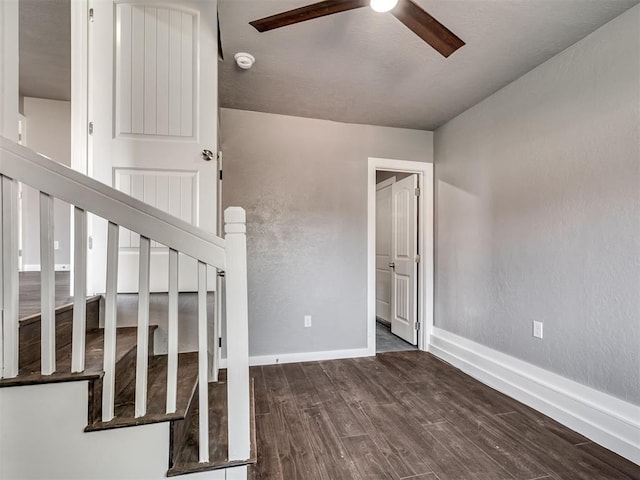 stairs featuring wood finished floors, a textured wall, baseboards, and ceiling fan