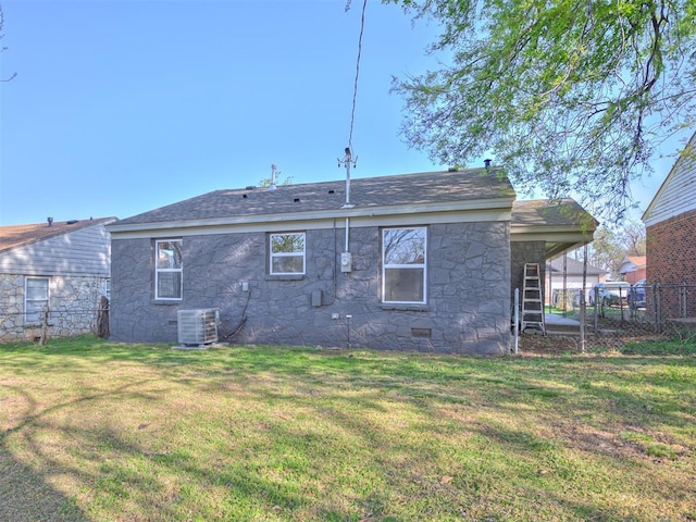 back of house with stone siding, central AC unit, fence, a lawn, and a shingled roof