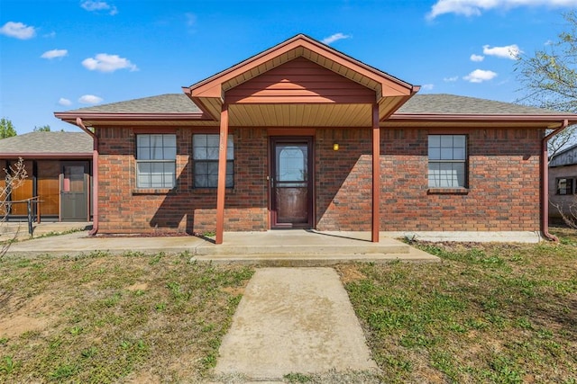 ranch-style house featuring brick siding, roof with shingles, and a front lawn