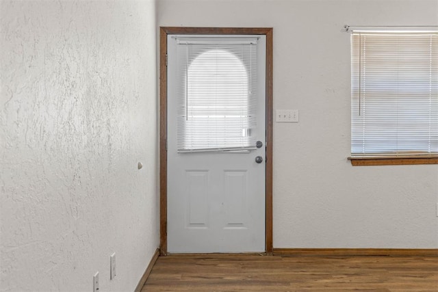 doorway with baseboards, wood finished floors, and a textured wall