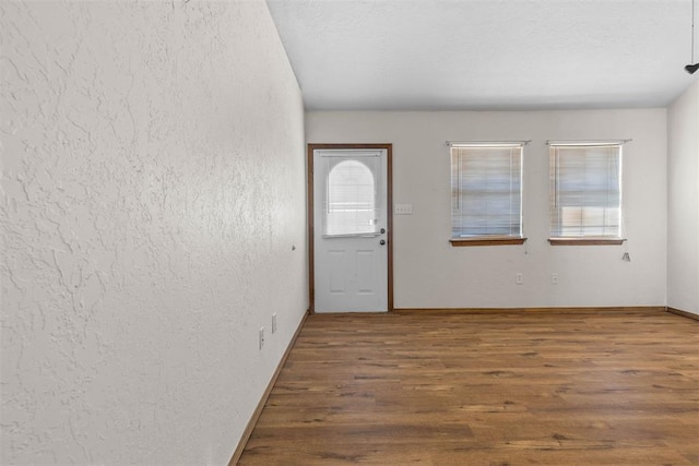 entryway featuring a textured wall, a textured ceiling, baseboards, and wood finished floors