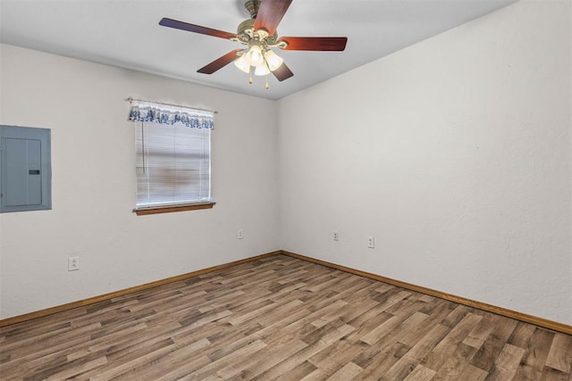 unfurnished room with baseboards, wood finished floors, electric panel, and a ceiling fan