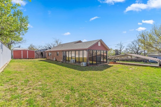 rear view of house featuring an outdoor structure, a carport, a sunroom, a storage unit, and a yard