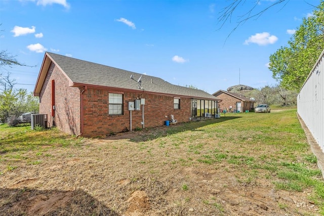 rear view of house featuring cooling unit, brick siding, roof with shingles, and a lawn