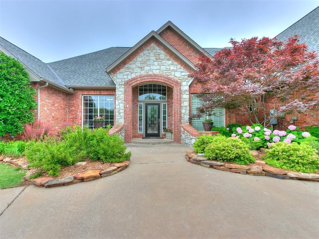 property entrance with stone siding, brick siding, and roof with shingles