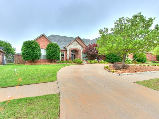 view of front facade featuring curved driveway, fence, a front yard, brick siding, and a shingled roof