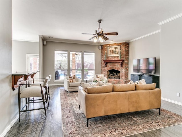 living room featuring crown molding, a ceiling fan, wood finished floors, a brick fireplace, and baseboards