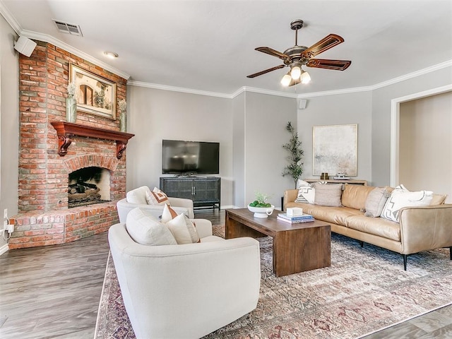 living room with visible vents, crown molding, a brick fireplace, wood finished floors, and a ceiling fan