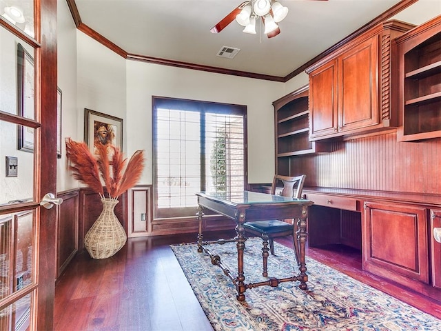 office featuring a wainscoted wall, visible vents, ceiling fan, ornamental molding, and dark wood finished floors