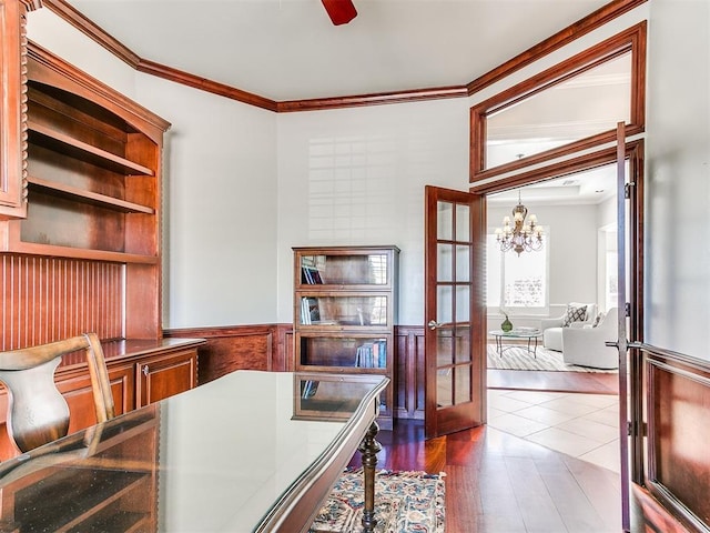 office featuring a wainscoted wall, crown molding, ceiling fan with notable chandelier, dark wood-style floors, and french doors