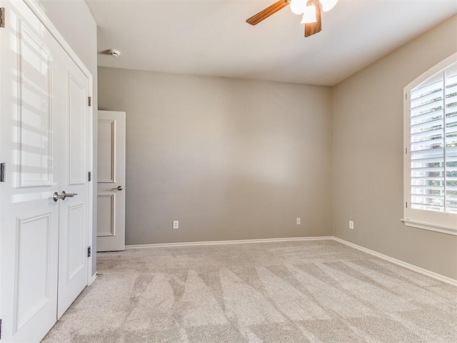 carpeted empty room with baseboards and a ceiling fan