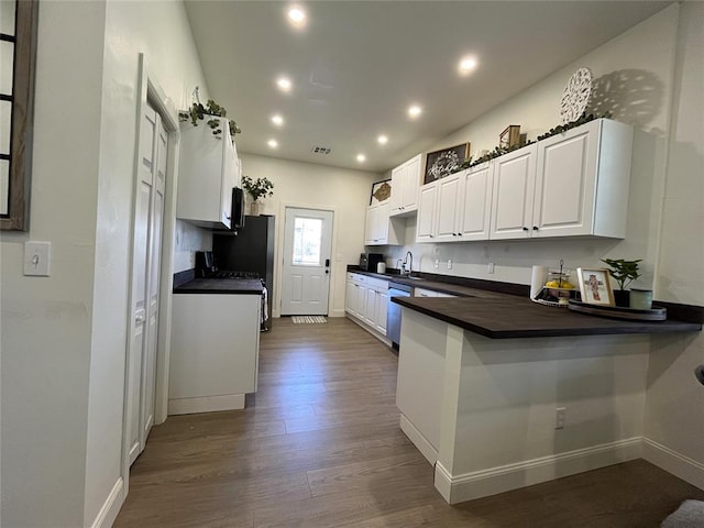 kitchen with recessed lighting, stainless steel dishwasher, dark countertops, dark wood-style floors, and a peninsula