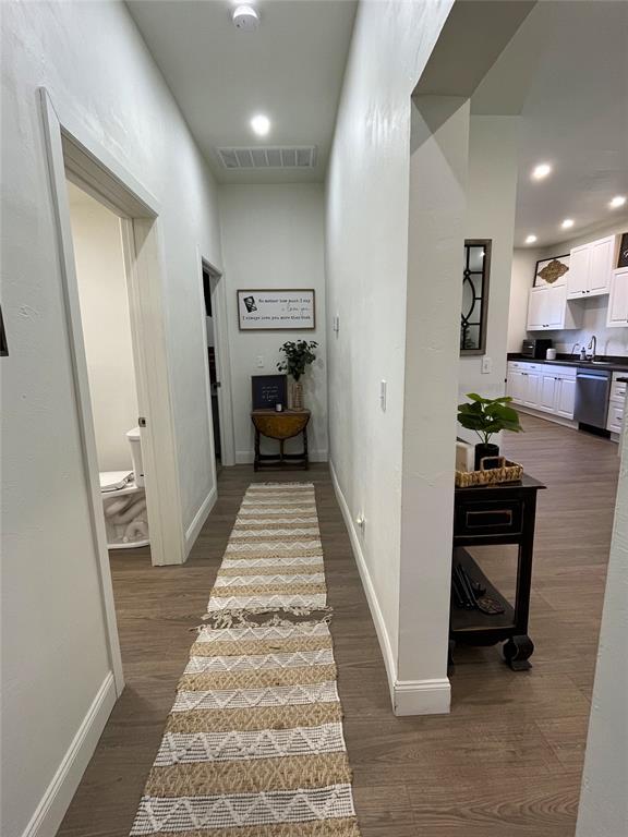 corridor with visible vents, baseboards, recessed lighting, dark wood-type flooring, and a sink