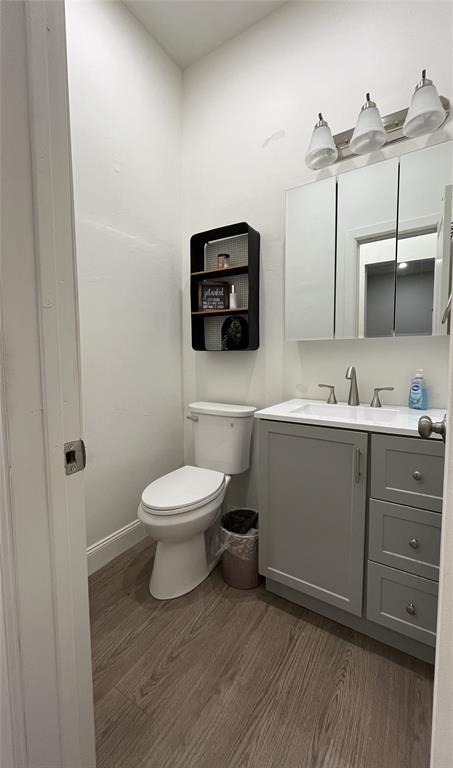 half bathroom with toilet, vanity, and wood finished floors