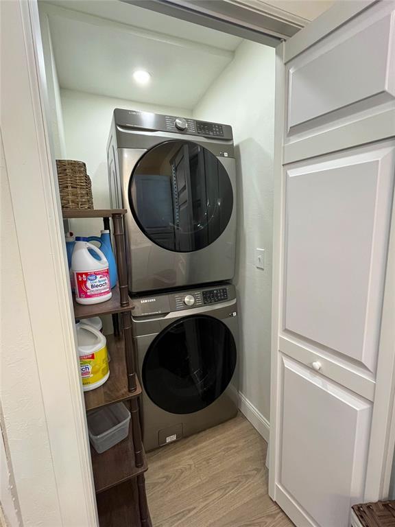 laundry room featuring baseboards, stacked washer / dryer, laundry area, and light wood-style floors