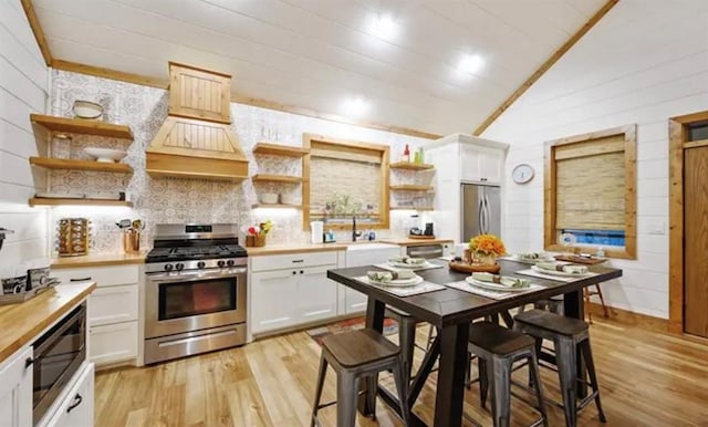 kitchen featuring light wood-style flooring, appliances with stainless steel finishes, lofted ceiling, and open shelves