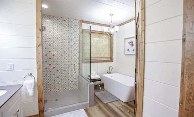 full bath with vanity, a shower stall, a freestanding bath, a notable chandelier, and wood finished floors