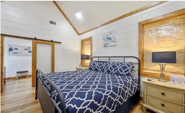 bedroom featuring a barn door, wooden walls, lofted ceiling, light wood-style flooring, and visible vents