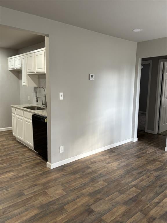 kitchen with dark wood-type flooring, black dishwasher, a sink, and baseboards