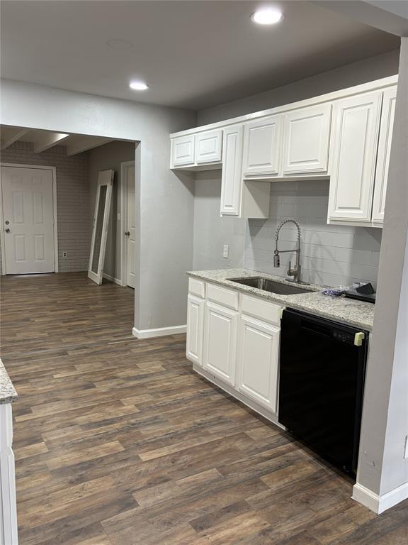 kitchen with baseboards, backsplash, dark wood-type flooring, dishwasher, and a sink