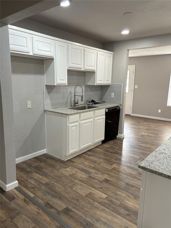kitchen featuring tasteful backsplash, white cabinetry, black dishwasher, a sink, and baseboards