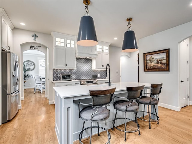 1924 Plaza District Dr, Edmond, OK 73034 - kitchen with light countertops, light wood-style floors, stainless steel fridge with ice dispenser, arched walkways, and decorative backsplash