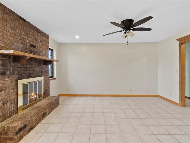 unfurnished living room with a ceiling fan, a brick fireplace, light tile patterned floors, and baseboards