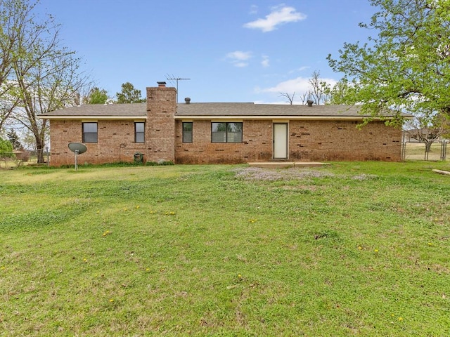 back of property with a chimney, fence, brick siding, and a yard