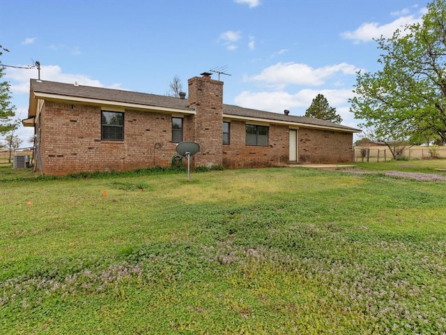 back of house with a lawn, a chimney, fence, and brick siding