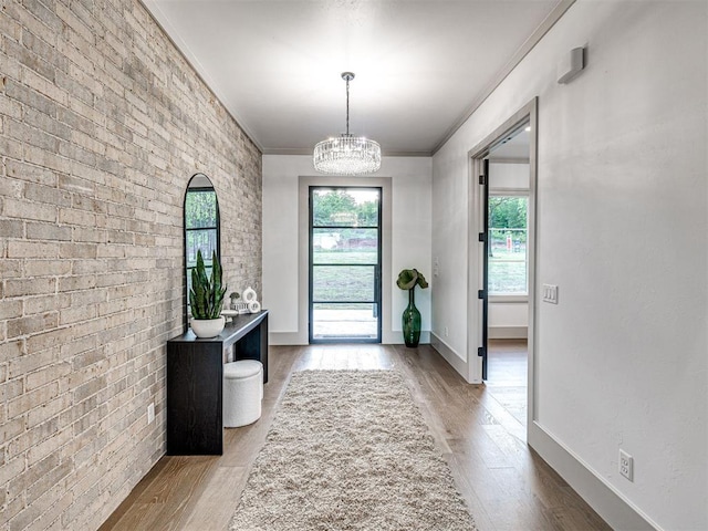 doorway with a chandelier, wood finished floors, baseboards, and ornamental molding
