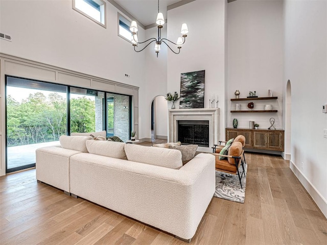 living area featuring visible vents, a towering ceiling, a chandelier, light wood-style floors, and a fireplace