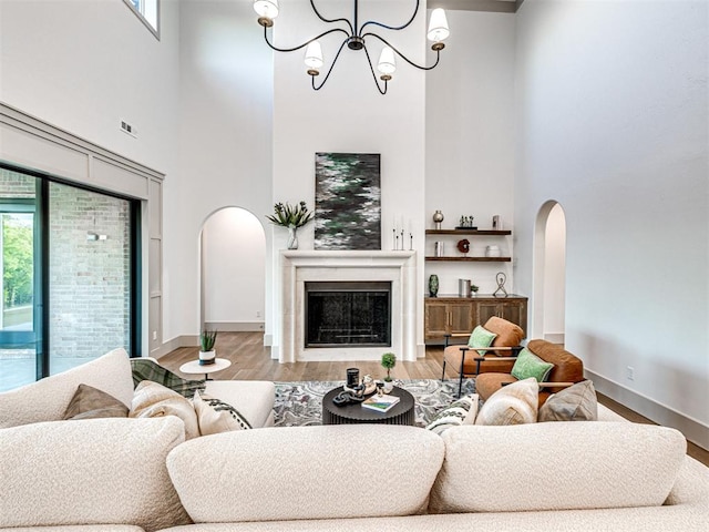 living room with arched walkways, baseboards, an inviting chandelier, wood finished floors, and a high ceiling