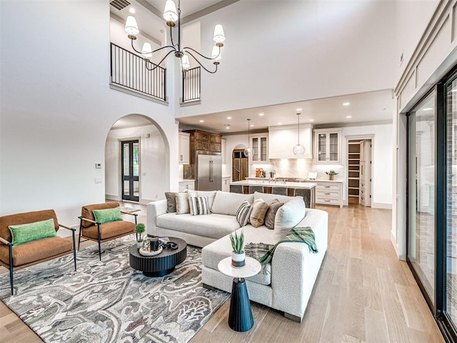 living area featuring light wood-style flooring, arched walkways, a towering ceiling, an inviting chandelier, and baseboards