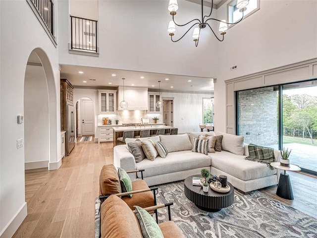 living room featuring arched walkways, baseboards, recessed lighting, a towering ceiling, and light wood-style floors