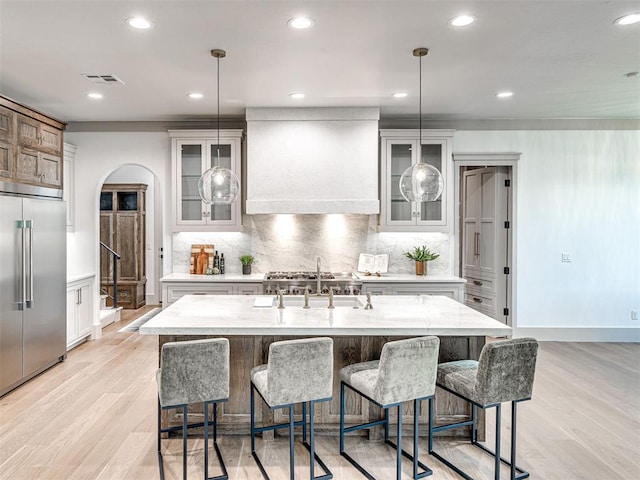 kitchen featuring a sink, light wood-style flooring, custom range hood, appliances with stainless steel finishes, and visible vents