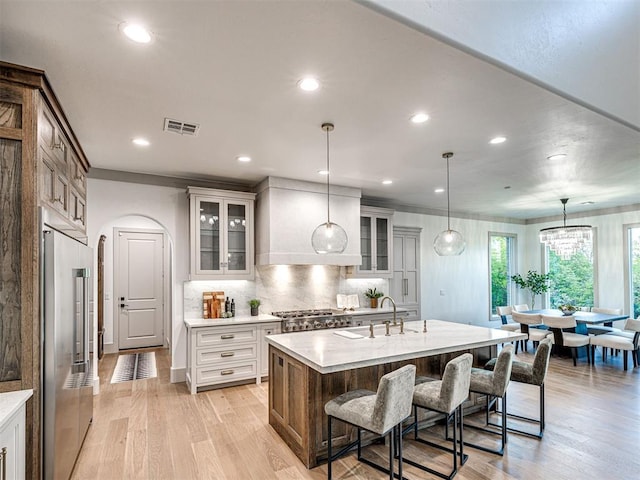 kitchen with light wood finished floors, custom exhaust hood, a sink, and high end refrigerator