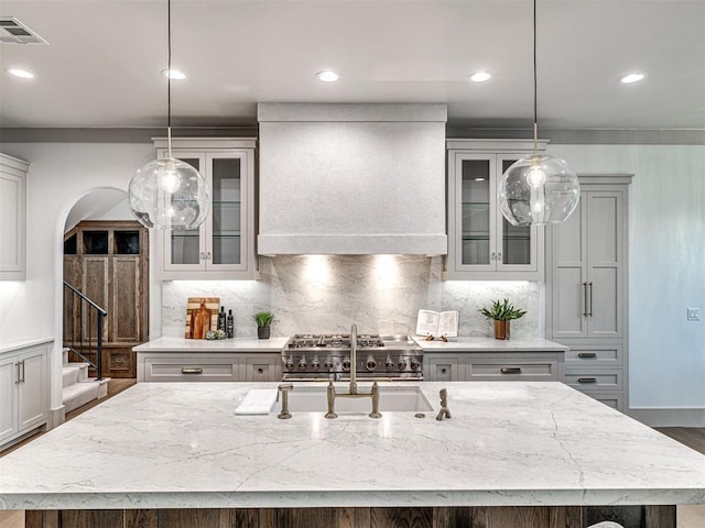 kitchen with light stone countertops, visible vents, custom exhaust hood, and glass insert cabinets