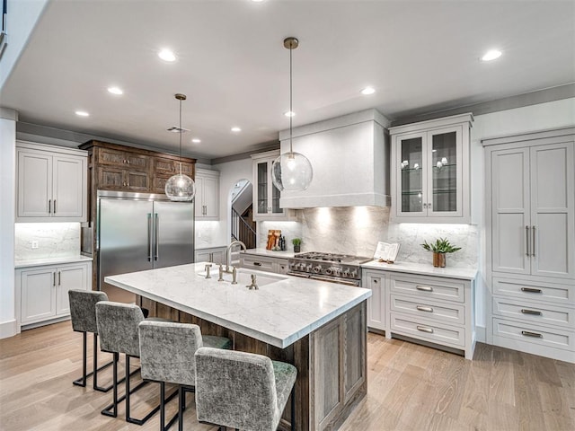 kitchen featuring recessed lighting, premium appliances, a sink, light wood-style floors, and custom exhaust hood