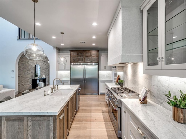 kitchen with backsplash, a sink, arched walkways, high quality appliances, and custom range hood