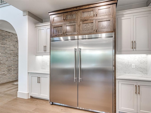 kitchen featuring light wood finished floors, stainless steel built in refrigerator, light stone counters, and tasteful backsplash