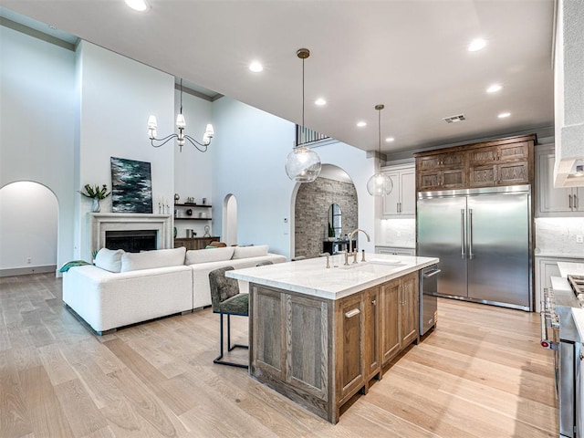 kitchen with a sink, light wood-style floors, arched walkways, stainless steel appliances, and visible vents