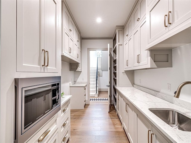 kitchen with stainless steel microwave, light wood finished floors, light stone counters, and a sink