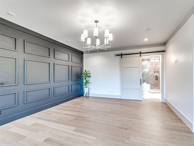 interior space featuring light wood-style flooring, baseboards, a chandelier, and a barn door