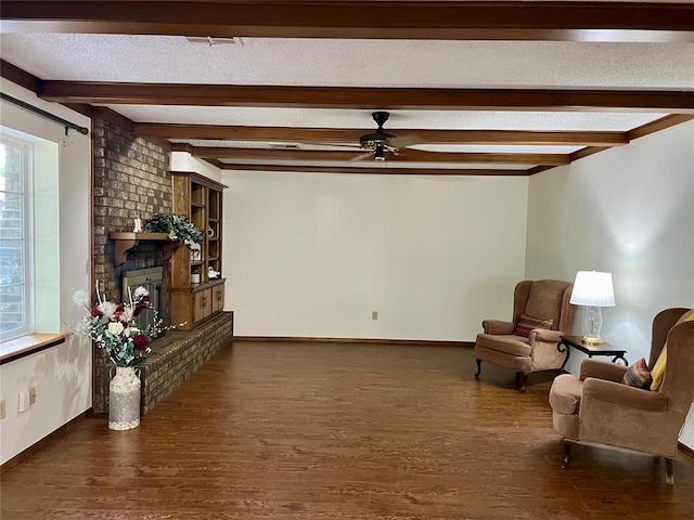 sitting room featuring a ceiling fan, dark wood finished floors, beam ceiling, baseboards, and a textured ceiling